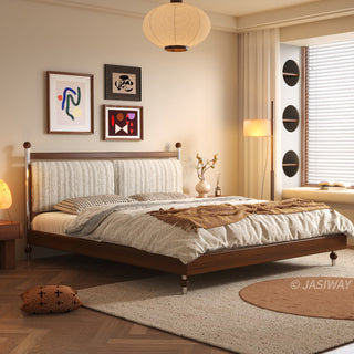 A warm, sunlit bedroom featuring a mid-century modern solid wood platform bed with a textured upholstered headboard, set against a wall with framed abstract art, a large paper pendant light, a cozy window nook with circular architectural details, and herringbone wood flooring.