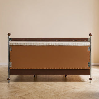 A rear-view studio shot of the bed frame, showcasing its clean construction, the smooth leather-upholstered panel on the back of the headboard, and the solid wood and metallic frame details, set against a simple wall and wood-look floor.