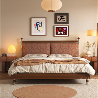 A frontal view of a mid-century modern solid wood platform bed with a woven terracotta upholstered headboard, styled with textured bedding, abstract wall art, and warm lighting from matching fluted nightstands with decorative accents.