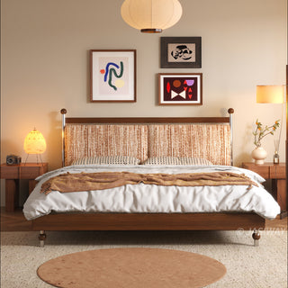 A frontal view of a mid-century modern solid wood platform bed with a textured tweed-like upholstered headboard in a rust-orange color, featuring warm ambient lighting from bedside lamps and a paper pendant light, all set in a decorated bedroom with three pieces of abstract wall art and a large textured rug.