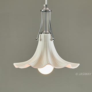 A white, ceramic pendant light hangs against a neutral grey background, featuring a graceful, fluted shade that resembles a blooming flower. A polished chrome fixture connects the ceramic shade to the ceiling, holding a single, glowing globe bulb at its center.