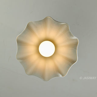 This direct, bottom-up view of the white, flower-shaped ceramic pendant light showcases its perfectly symmetrical, fluted design. A single, glowing bulb sits at the center, casting a soft, radiating light across the interior ridges of the shade. The minimalist composition emphasizes the organic, petal-like form of the fixture.