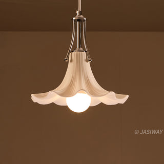 A white, ceramic pendant light hangs against a warm brown background, featuring a gracefully fluted shade that resembles a blooming flower. A polished chrome fixture connects the ceramic shade to the ceiling, holding a single, illuminated globe bulb at its center.