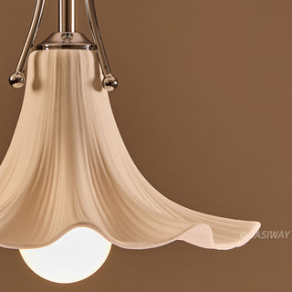 A close-up view highlights the delicate texture and organic form of the white, ceramic, flower-shaped pendant shade. A polished chrome metal holder attaches the ceramic piece, while a portion of an illuminated white bulb is visible beneath. The warm, solid brown background emphasizes the smooth, fluted details of the design.