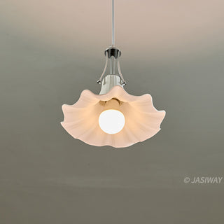 A white, flower-shaped ceramic pendant light is captured from below, showcasing the interior of its fluted shade against a neutral grey background. The central bulb emits a soft glow, illuminating the delicate ridges of the ceramic structure. A polished chrome fixture secures the light.