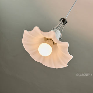 A low-angle view captures the white, flower-shaped ceramic pendant light from an angled perspective. The central illuminated bulb casts a gentle light onto the fluted, organic curves of the shade. A sleek, polished chrome fixture secures the piece.