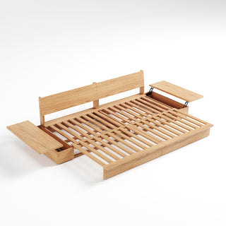 A studio product shot displays an extended light wood sofa bed frame against a plain white background. The frame features a slatted wooden sleeping surface and two upright backrest panels. Attached side tables feature hinged lids, with both lids lifted open to reveal storage compartments underneath.