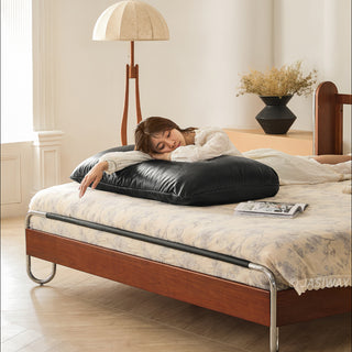 JASIWAY luxury minimalist platform bed with solid wood frame integrated with a curved chrome stainless steel tubular structure, featuring an ergonomic dual-pillow cushioned headboard upholstered in premium black leather, blending mid-century modern craftsmanship with industrial elegance, celebrated as the London Design Awards 2025 Silver Winner for master bedroom furniture design.-Medium shot with model lying on the upholstered headboard