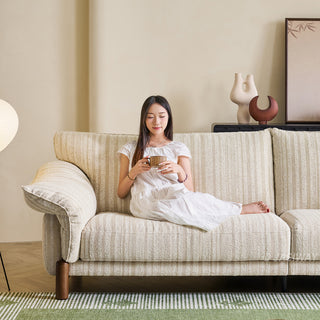 JASIWAY modern 3-seater sofa featuring a premium striped upholstery with deep-seated comfort, plush oversized cushions, flared armrests and solid wood legs in a dark walnut finish, showcasing a minimalist Japandi and organic modern aesthetic. -Front view with model sitting and relaxing