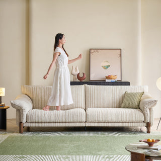 JASIWAY modern 3-seater sofa featuring a premium striped upholstery with deep-seated comfort, plush oversized cushions, flared armrests and solid wood legs in a dark walnut finish, showcasing a minimalist Japandi and organic modern aesthetic. -Front view with model standing