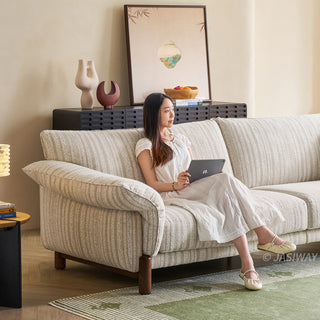 JASIWAY modern 3-seater sofa featuring a premium striped upholstery with deep-seated comfort, plush oversized cushions, flared armrests and solid wood legs in a dark walnut finish, showcasing a minimalist Japandi and organic modern aesthetic. -Diagonal view with model sitting