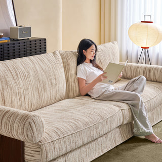 JASIWAY textured linen blend sofa, featuring a minimalist upholstery with a subtle linear weave, highlighting its plush, oversized bolsters and the architectural solid wood side panels, perfect for contemporary living rooms.-Diagonal view with model sitting