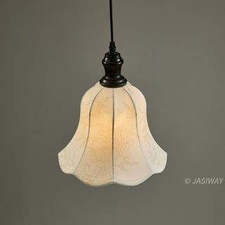 A vintage-style pendant lamp hangs illuminated against a solid, neutral grey background. The bell-shaped fabric shade features a delicate, light-colored floral and vine pattern with subtle scalloped edges. It is suspended by a dark, aged bronze-finish fixture and a black cord.