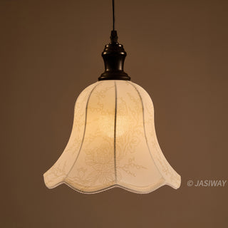 This elegant pendant light features a scalloped, bell-shaped fabric shade detailed with a subtle, intricate floral pattern. The shade diffuses light to cast a warm, inviting glow, perfectly complemented by a minimalist dark-toned fixture. Its design beautifully balances classic charm with understated, artisanal sophistication for a curated interior space.