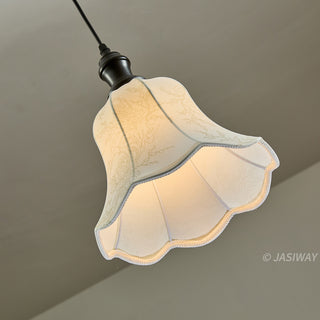 This elegant pendant light features a scalloped, bell-shaped fabric shade adorned with a subtle, intricate floral pattern. The shade diffuses light to cast a warm, inviting glow, complemented by a simple, dark-toned fixture. Its design balances classic charm with understated elegance, making it a refined lighting choice for a curated interior.