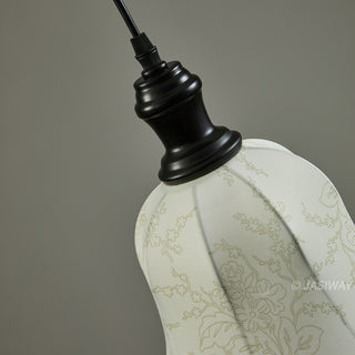 A close-up view shows the elegant connection between the minimalist black fixture and the bell-shaped fabric shade of this pendant light. The light-colored fabric features a delicate, intricate floral pattern that highlights the artisanal quality and attention to detail. This refined design offers a perfect balance of classic charm and understated modern style for a curated interior.