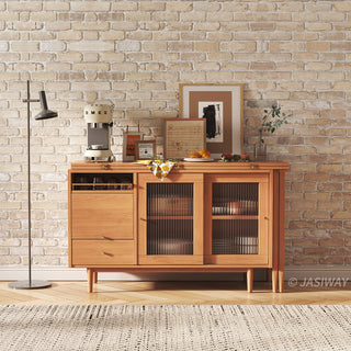 Wide-angle lifestyle shot of a modern natural wood sideboard cabinet with fluted glass doors and a coffee bar setup against an exposed brick wall.