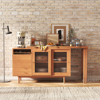 Wide-angle lifestyle shot of a modern natural wood sideboard cabinet with fluted glass sliding doors, staged against an exposed brick wall with a coffee station and framed artwork.