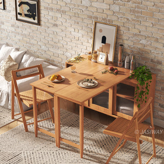 Lifestyle shot of a modern natural wood extendable dining table set with matching folding chairs, staged in a cozy apartment with an exposed brick wall and tableware.