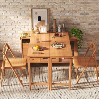 Top-down lifestyle shot of a modern natural wood extendable dining table set with matching folding chairs, staged on a textured rug against an exposed brick wall.