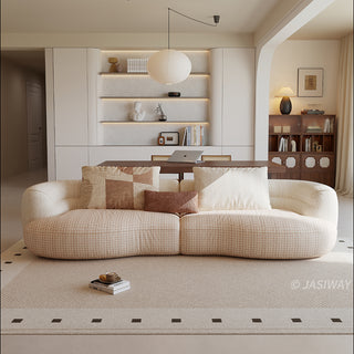 A beige textured modern curved sectional sofa featuring low-profile seating and matching back cushions, placed in a contemporary living room with a neutral area rug and built-in shelving.