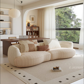 A beige textured modern curved sectional sofa featuring low-profile seating and matching back cushions, placed in a contemporary living room with a neutral area rug and built-in shelving.