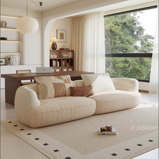 A beige textured modern curved sectional sofa featuring low-profile seating and matching back cushions, placed in a contemporary living room with a neutral area rug and built-in shelving.