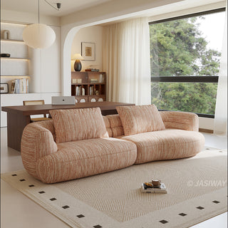A beige textured modern curved sectional sofa featuring low-profile seating and matching back cushions, placed in a contemporary living room with a neutral area rug, a wooden dining table, and large windows.