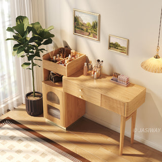 High-angle lifestyle view of a modern wooden vanity desk with fluted storage, organized cosmetics, and a potted plant in a warm bedroom setting.