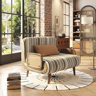 Modern convertible accent chair with green and olive striped upholstery, woven rattan armrests, and a brown lumbar pillow, styled on a geometric round rug in a sunny loft living room with brick wall accents and French windows.
