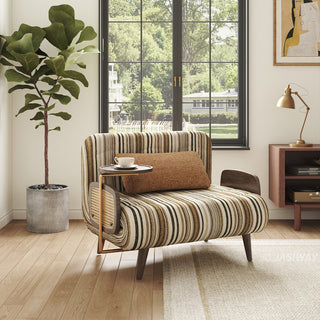 Front level view of a modern striped accent chair with brown lumbar pillow, side swiveling coffee tray table, rattan side panels, and dark wood legs, styled in a bright living room near a window and large potted plant.