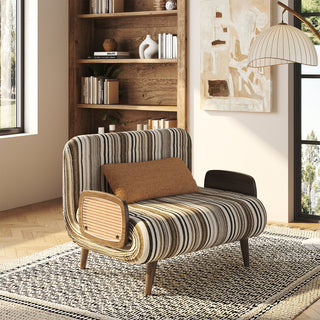 Modern convertible accent chair in green and cream striped bouclé fabric, featuring woven rattan armrest panels, a brown lumbar pillow, and solid wood legs, styled on a patterned area rug in a sunlit room with a wooden bookshelf and arch floor lamp.