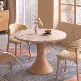 Modern Japandi round dining table featuring a beige marble top and wooden hourglass pedestal base set with textured dining chairs on a geometric area rug.