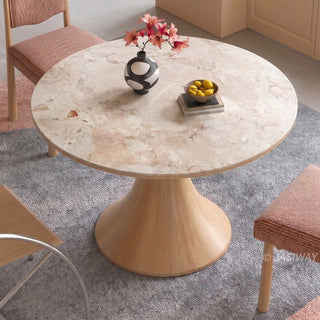 High-angle view of a modern Japandi smooth round marble dining table with a flared wooden pedestal base, styled with pink upholstered dining chairs   