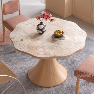 High-angle view of a modern Japandi round dining table with a scalloped wave-edge marble top and flared wooden pedestal base, styled with pink upholstered chairs.