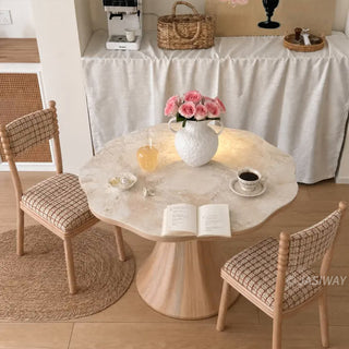 High-angle view of a modern French cream style scalloped wave-edge marble round bistro dining table with two plaid upholstered chairs in a cozy coffee nook.