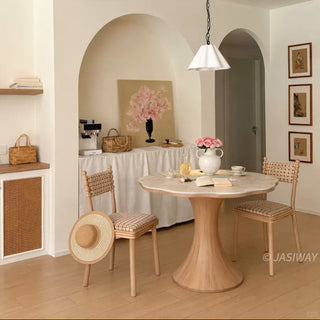 Wide-angle view of a modern French cream style scalloped wave-edge marble round bistro dining table with a wooden pedestal base and plaid chairs in a double-arched dining room.