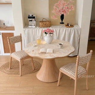 Modern French cream style scalloped wave-edge round marble bistro dining table with a wooden pedestal base and two plaid upholstered chairs in a cozy coffee nook.