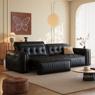 A modern black leather sofa is placed in a warmly lit, minimalist living room. The sofa features a tufted backrest, a patterned throw pillow, and a pulled-out section to form a lounge. A wooden coffee table sits on a rug in the foreground, while a framed butterfly artwork and a spherical pendant lamp decorate the background.