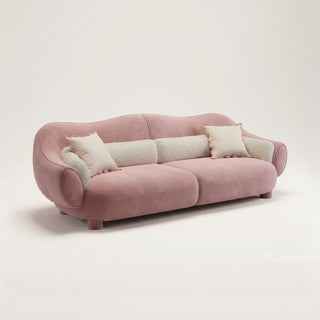 RINGCHEN modern luxury blush pink curved cloud sofa featuring a sculptural shell-inspired silhouette, premium deep-seat upholstered velvet fabric with decorative cream boucle lumbar pillows and ruffled accent cushions for a high-end designer living room aesthetic.-Three quarter studio view