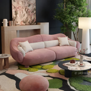 RINGCHEN modern luxury blush pink curved cloud sofa featuring a sculptural shell-inspired silhouette, premium deep-seat upholstered velvet fabric with decorative cream boucle lumbar pillows and ruffled accent cushions for a high-end designer living room aesthetic.-Three quarter view