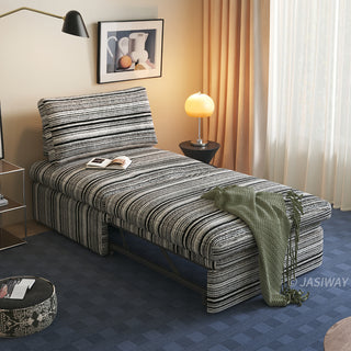A black and white striped sherpa convertible sleeper sofa bed is fully extended in a modern living room, styled with a green throw blanket, open book, and warm ambient lighting.