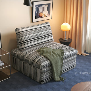 A black and white striped sherpa convertible sleeper sofa is styled as an armchair in a cozy living room, draped with a green throw blanket and accented by warm lighting.