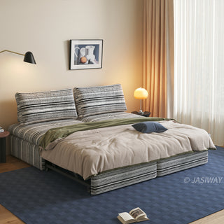 A black and white striped sherpa double convertible sleeper sofa is fully expanded into a spacious bed, styled in a warm living room with layered bedding, a blue accent pillow, and soft ambient lighting.