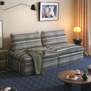 A black and white striped sherpa double convertible sleeper sofa is styled in a cozy living room, draped with a green throw blanket and set against warm ambient lighting.