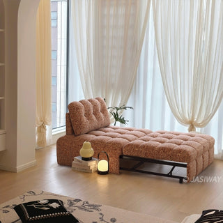 A rust red tufted chenille convertible sleeper sofa is styled in a bright, sunlit living room with sheer white curtains and decorative floor lighting.