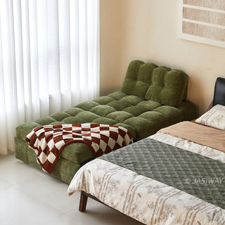 An olive green tufted chenille convertible sleeper sofa bed is set up next to a bed in a bright, modern bedroom, styled with a brown and white checkered throw blanket.