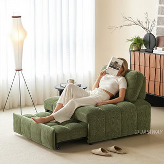 A young woman reads a book while relaxing on an olive green tufted chenille convertible sleeper sofa bed fully extended in a bright, modern living room.
