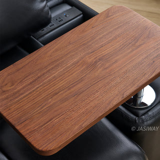 A high-angle close-up showcases a rich wooden swivel tray attached to a modern black leather sofa. The smooth wooden tabletop features a natural grain pattern, mounted on a polished chrome support stem. In the background, built-in power outlets are integrated into the sofa's armrest structure.
