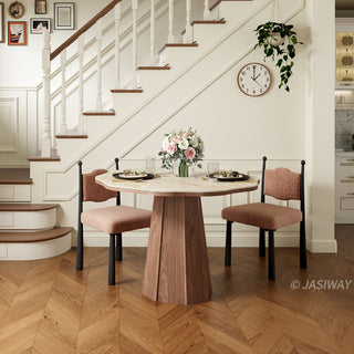 Lifestyle shot of a modern round sintered stone dining table with a faceted wooden pedestal base, paired with textured upholstered dining chairs and place settings near a staircase in a warm residential dining room.